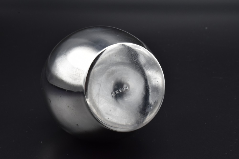 A small, bulbous sterling silver miniature tea caddy with a fitted lid, round ball finial, and visible British hallmarks stamped around the neck. View VI