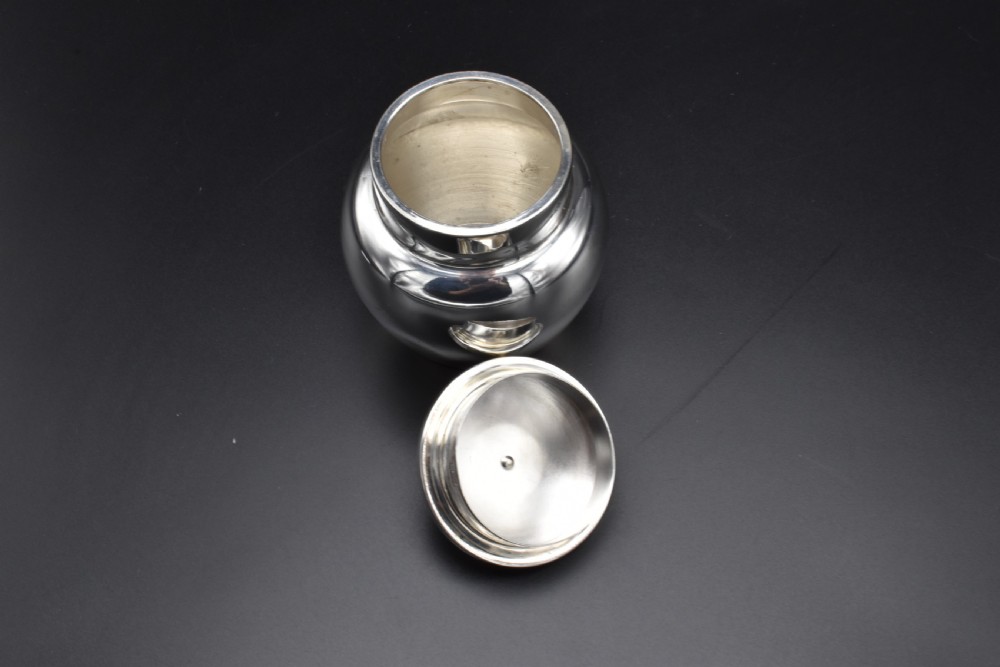 A small, bulbous sterling silver miniature tea caddy with a fitted lid, round ball finial, and visible British hallmarks stamped around the neck. View VIII
