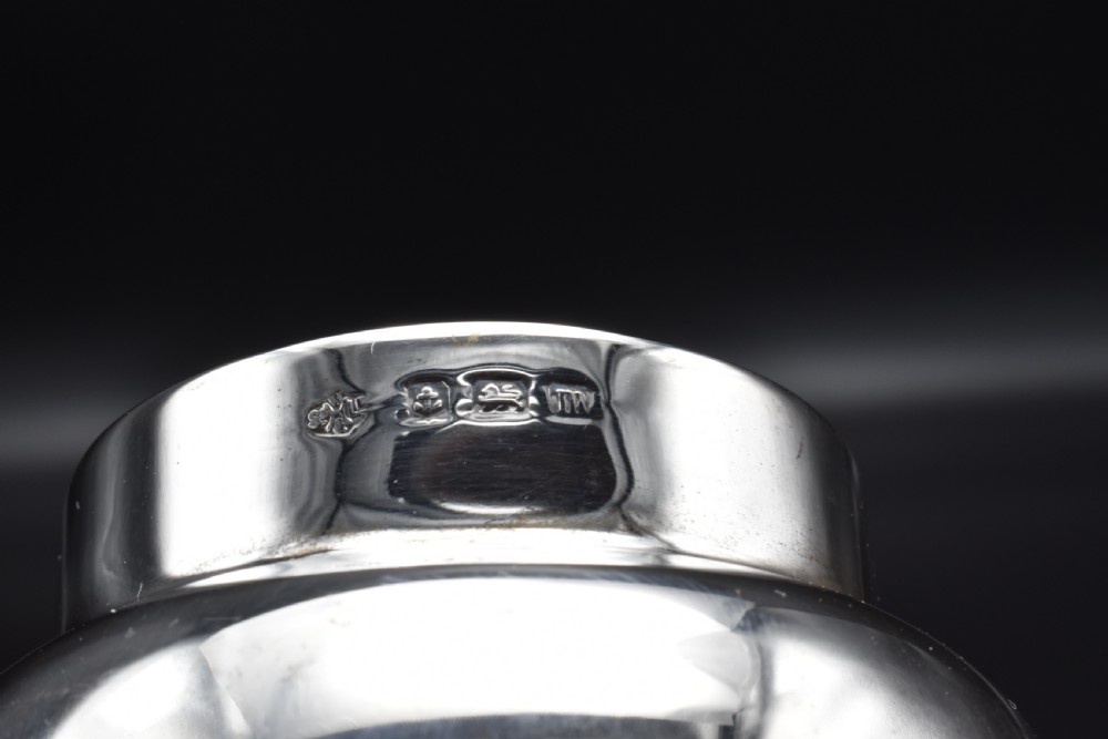 A small, bulbous sterling silver miniature tea caddy with a fitted lid, round ball finial, and visible British hallmarks stamped around the neck. View X