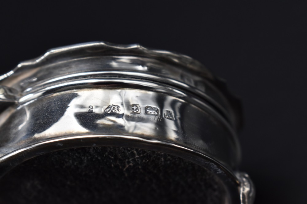 A circular sterling silver dressing table box with a shaped rim and cabriole feet displayed on a dark surface. View IV