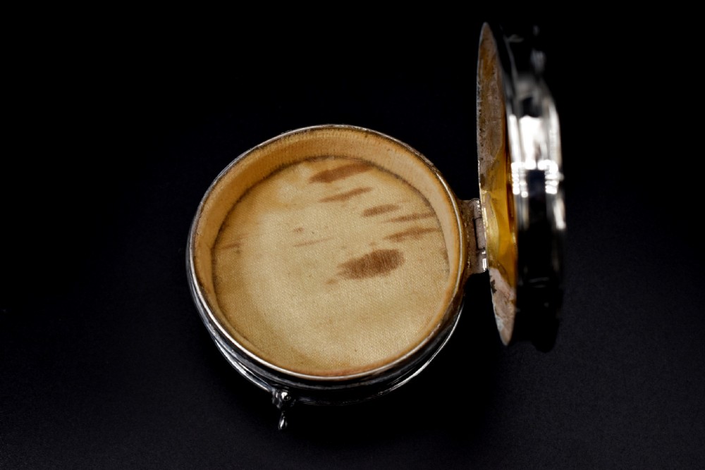 A circular sterling silver dressing table box with a shaped rim and cabriole feet displayed on a dark surface. View VII