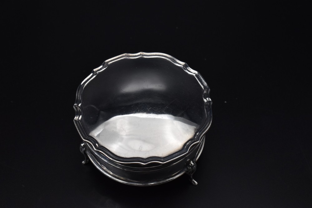 A circular sterling silver dressing table box with a shaped rim and cabriole feet displayed on a dark surface. View VIII