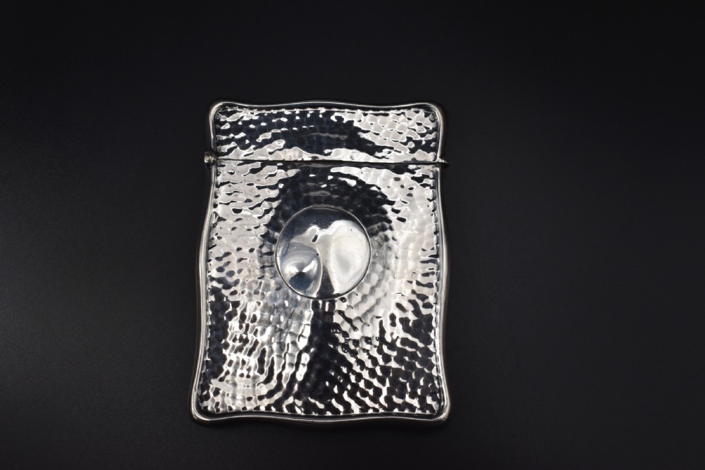 A hinged Edwardian sterling silver card case featuring a spot-hammered textured surface and a smooth circular central cartouche.