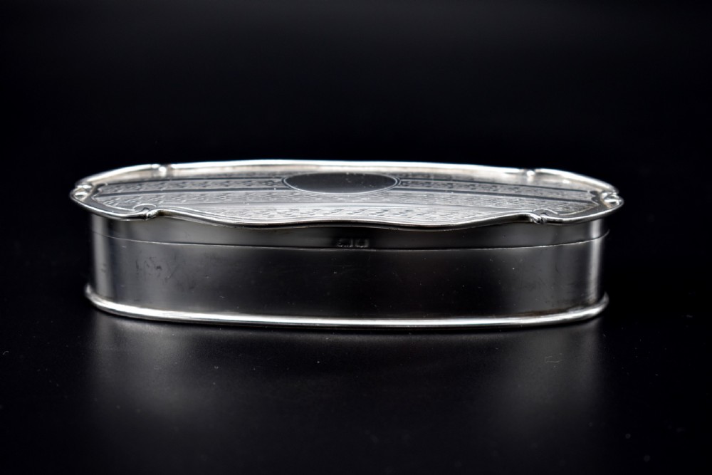 An elongated, oval Edwardian sterling silver powder box featuring engine-turned engraving on the lid and an unengraved central cartouche. View III