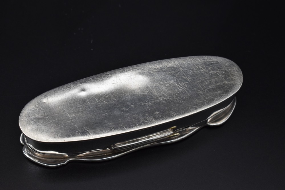 An elongated, oval Edwardian sterling silver powder box featuring engine-turned engraving on the lid and an unengraved central cartouche. View VI