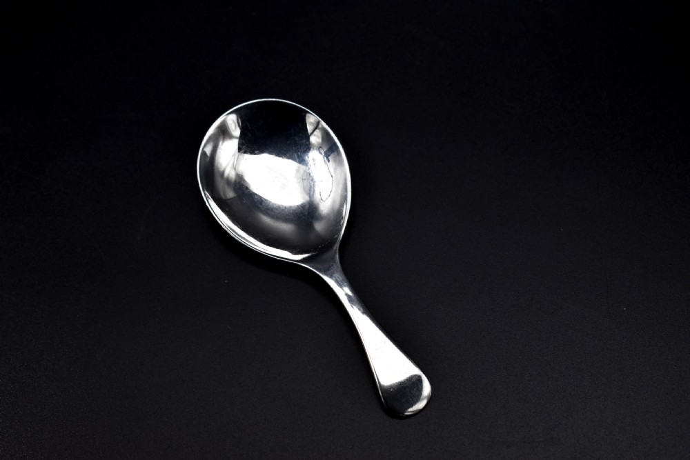 A late Victorian sterling silver caddy spoon featuring a plain oval bowl and a short flared handle against a dark background.