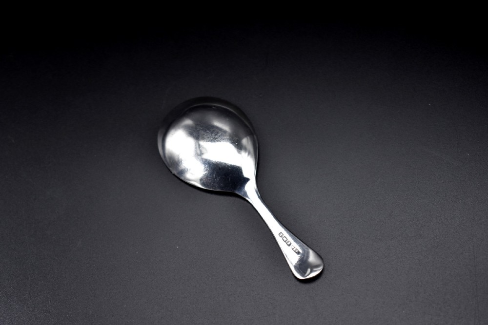 A late Victorian sterling silver caddy spoon featuring a plain oval bowl and a short flared handle against a dark background. View II