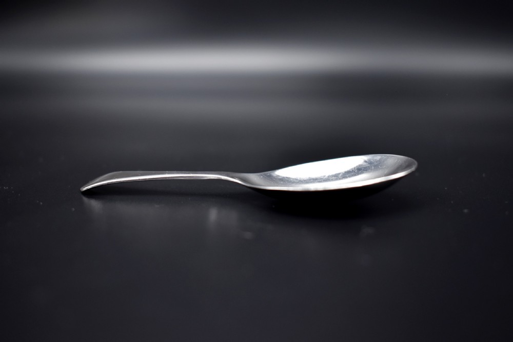 A late Victorian sterling silver caddy spoon featuring a plain oval bowl and a short flared handle against a dark background. View IV