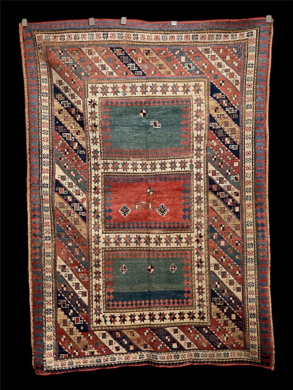 An antique hand-knotted Caucasian Bordjalou Kazak wool rug featuring three rectangular central panels surrounded by geometric diagonal borders in terracotta red, teal, cream, and blue.