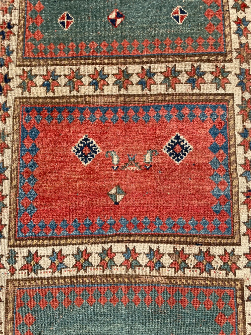 An antique hand-knotted Caucasian Bordjalou Kazak wool rug featuring three rectangular central panels surrounded by geometric diagonal borders in terracotta red, teal, cream, and blue. View X