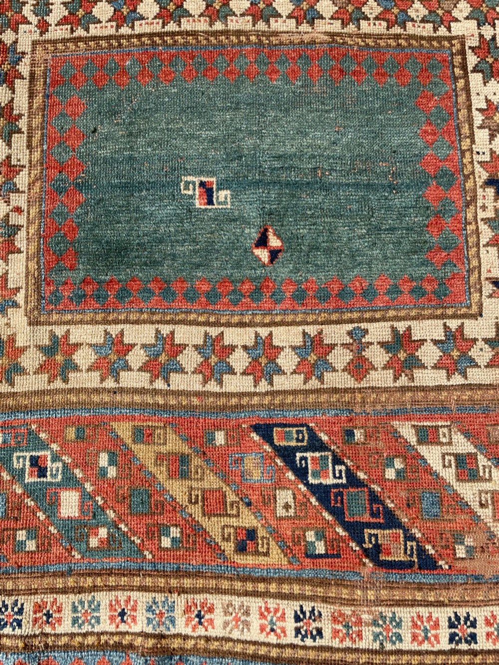 An antique hand-knotted Caucasian Bordjalou Kazak wool rug featuring three rectangular central panels surrounded by geometric diagonal borders in terracotta red, teal, cream, and blue. View XI