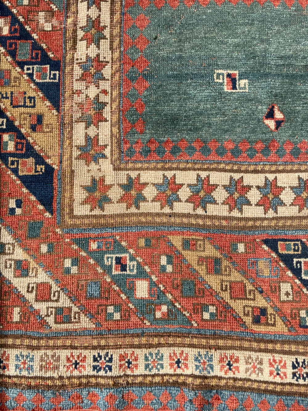 An antique hand-knotted Caucasian Bordjalou Kazak wool rug featuring three rectangular central panels surrounded by geometric diagonal borders in terracotta red, teal, cream, and blue. View XIII