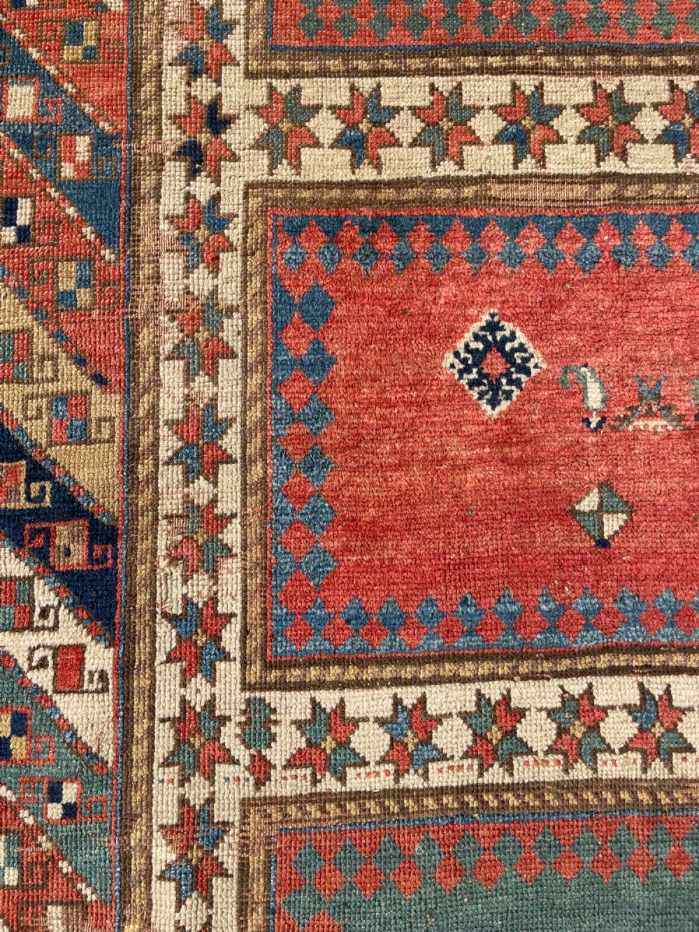 An antique hand-knotted Caucasian Bordjalou Kazak wool rug featuring three rectangular central panels surrounded by geometric diagonal borders in terracotta red, teal, cream, and blue. View XIV