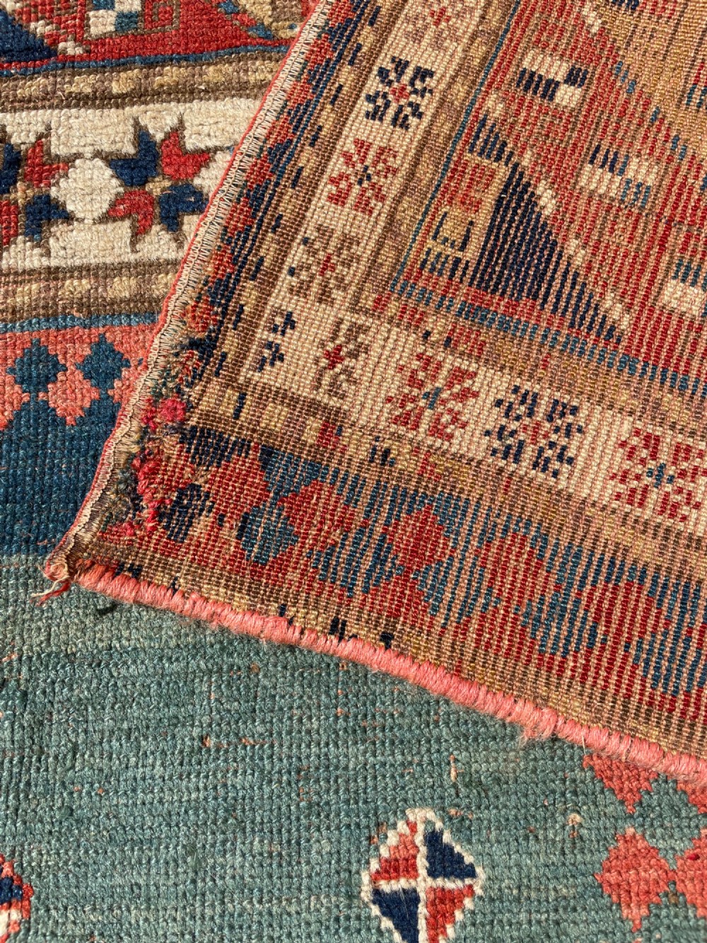 An antique hand-knotted Caucasian Bordjalou Kazak wool rug featuring three rectangular central panels surrounded by geometric diagonal borders in terracotta red, teal, cream, and blue. View XV