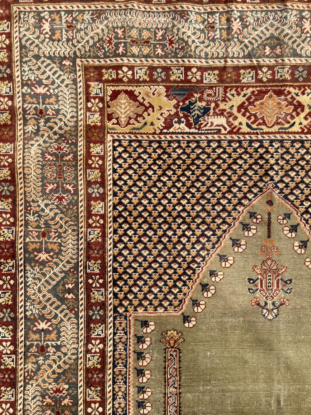 An antique hand-knotted Anatolian Ghiordes prayer rug featuring a central sage green arched niche enclosed by detailed rust red and blue decorative borders. View IX