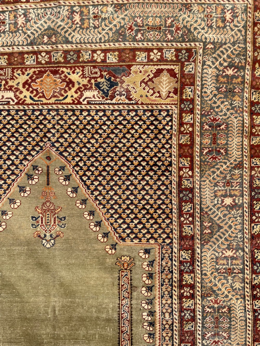 An antique hand-knotted Anatolian Ghiordes prayer rug featuring a central sage green arched niche enclosed by detailed rust red and blue decorative borders. View X