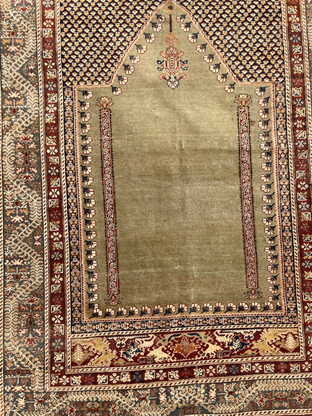 An antique hand-knotted Anatolian Ghiordes prayer rug featuring a central sage green arched niche enclosed by detailed rust red and blue decorative borders. View XII