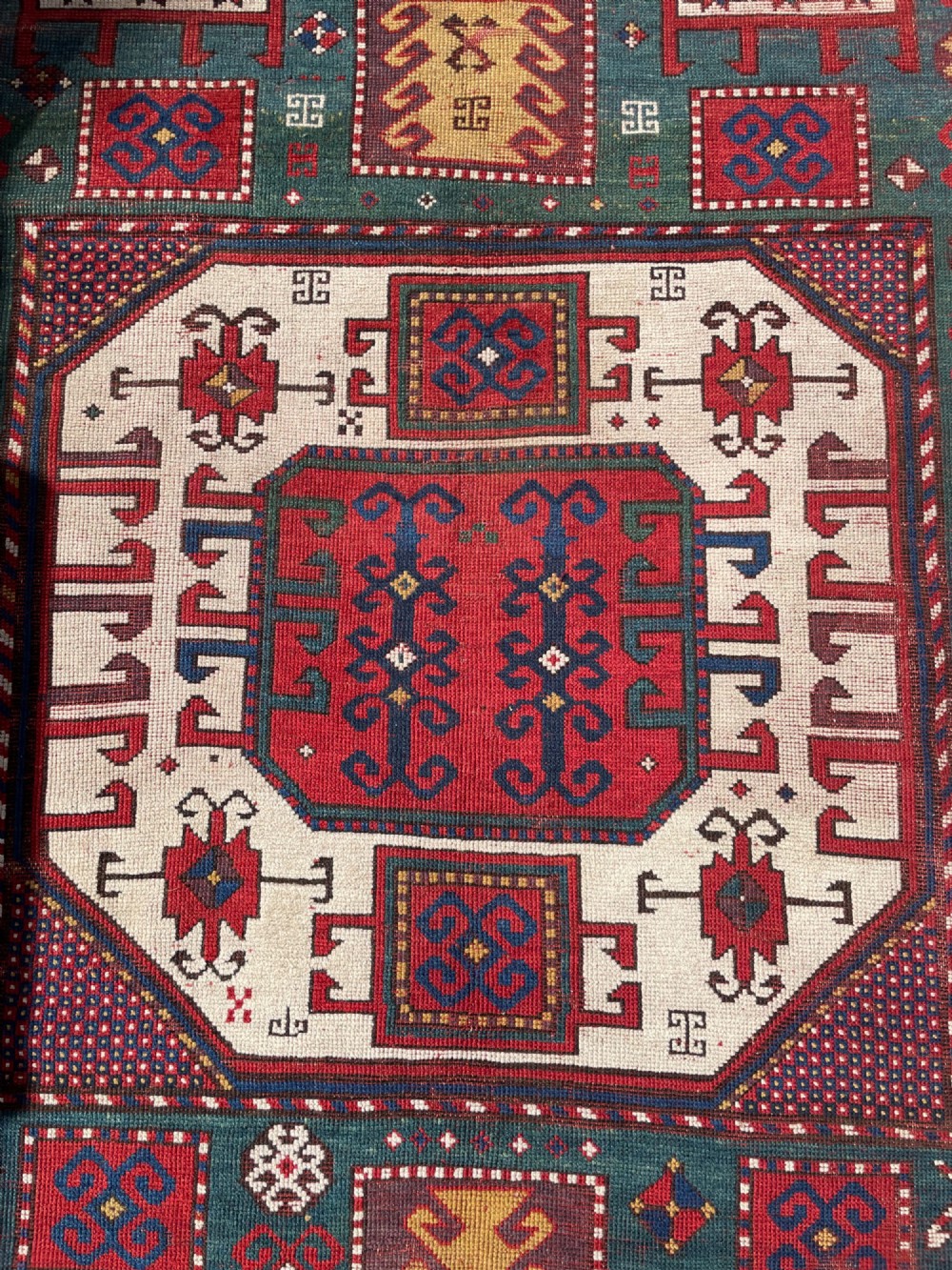 An antique Caucasian Karachov wool rug featuring a central ivory octagonal medallion surrounded by geometric star motifs in red, teal blue, and yellow. View XII