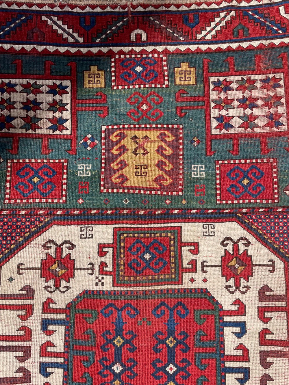 An antique Caucasian Karachov wool rug featuring a central ivory octagonal medallion surrounded by geometric star motifs in red, teal blue, and yellow. View XIII