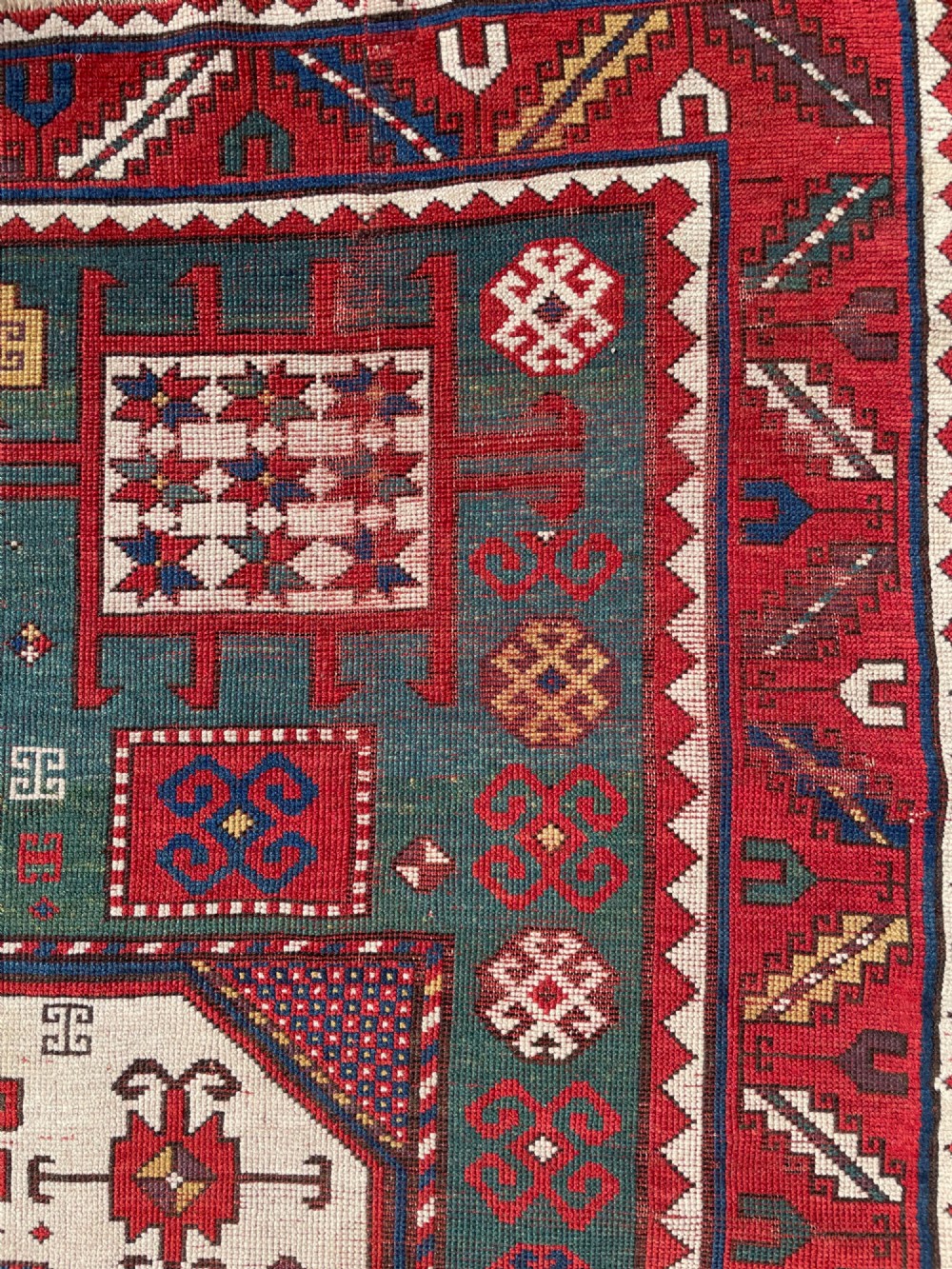 An antique Caucasian Karachov wool rug featuring a central ivory octagonal medallion surrounded by geometric star motifs in red, teal blue, and yellow. View XIV