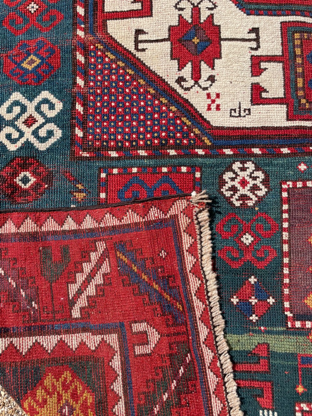 An antique Caucasian Karachov wool rug featuring a central ivory octagonal medallion surrounded by geometric star motifs in red, teal blue, and yellow. View XV