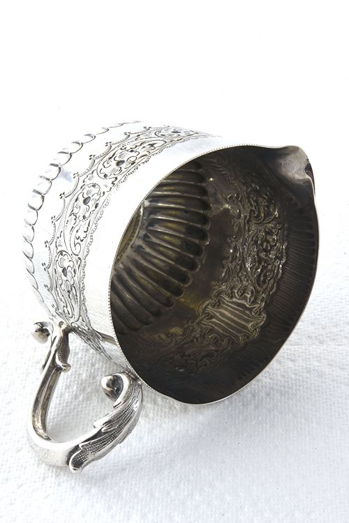 fig 2. A late Victorian sterling silver cream jug featuring detailed floral scroll chasing along the upper body, lower fluted gadrooning, and a curved handle.