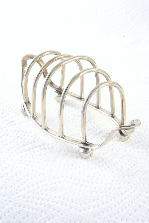 fig 1. A 1939 sterling silver four-slice toast rack featuring curved wire arches, raised ball feet, and visible hallmarking.