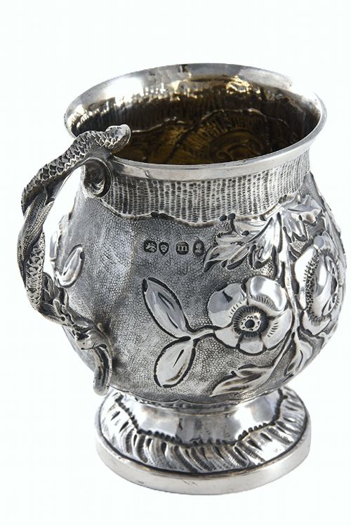 fig 1. A George IV sterling silver christening mug with floral repousse work, a plain cartouche, and a curved handle set on a stepped base.