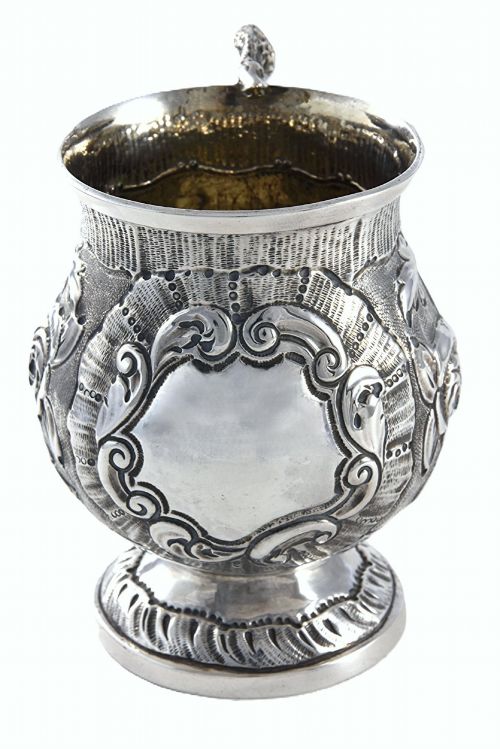 fig 2. A George IV sterling silver christening mug with floral repousse work, a plain cartouche, and a curved handle set on a stepped base.