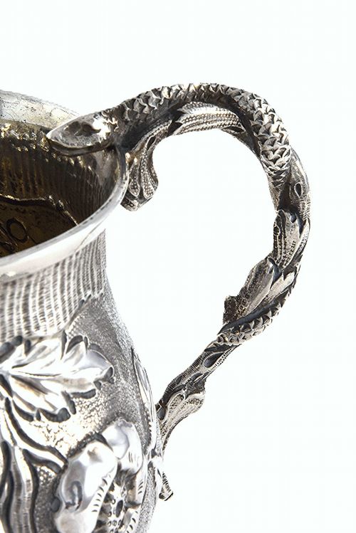 fig 4. A George IV sterling silver christening mug with floral repousse work, a plain cartouche, and a curved handle set on a stepped base.