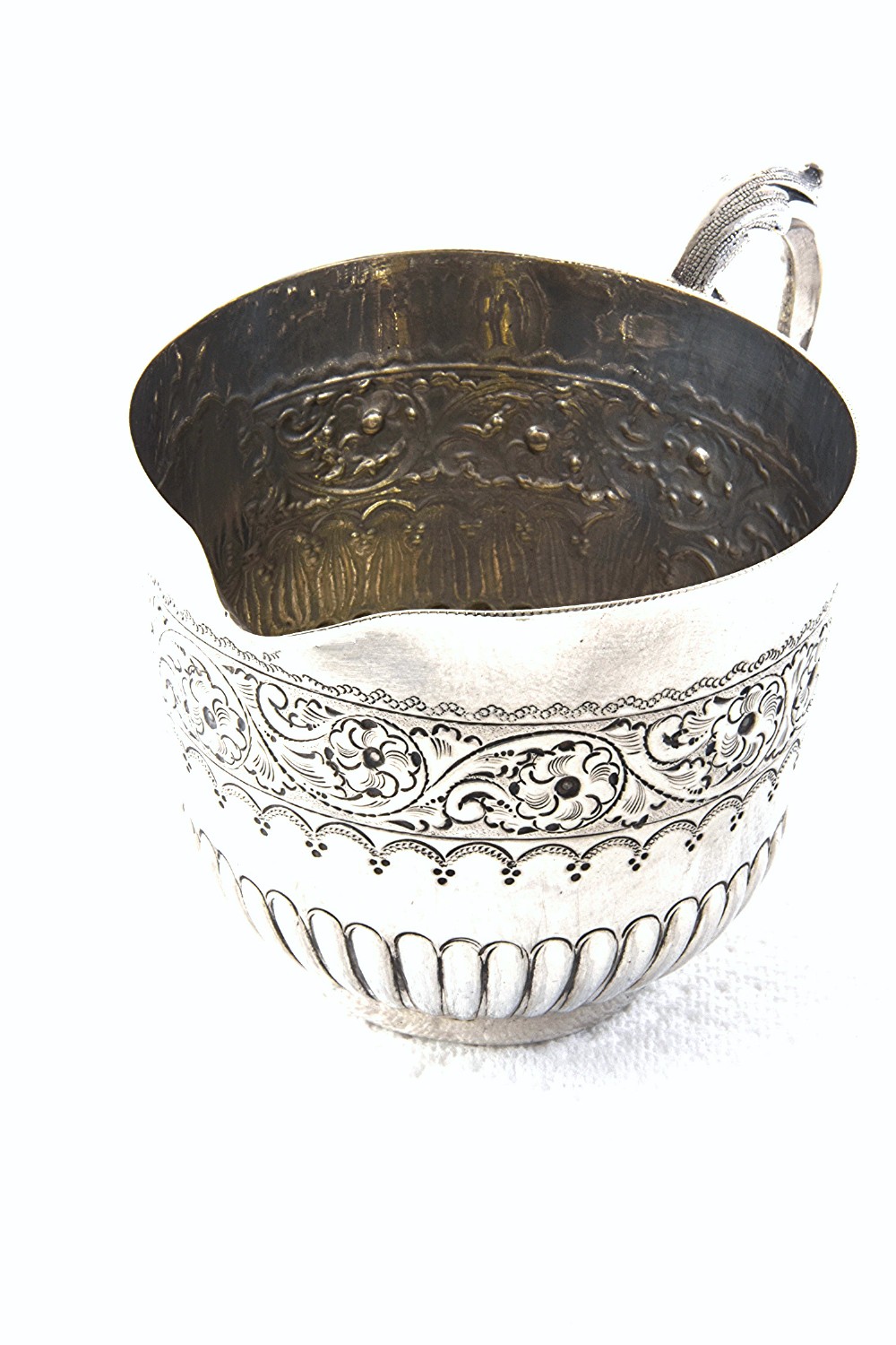 A late Victorian sterling silver cream jug featuring detailed floral scroll chasing along the upper body, lower fluted gadrooning, and a curved handle.