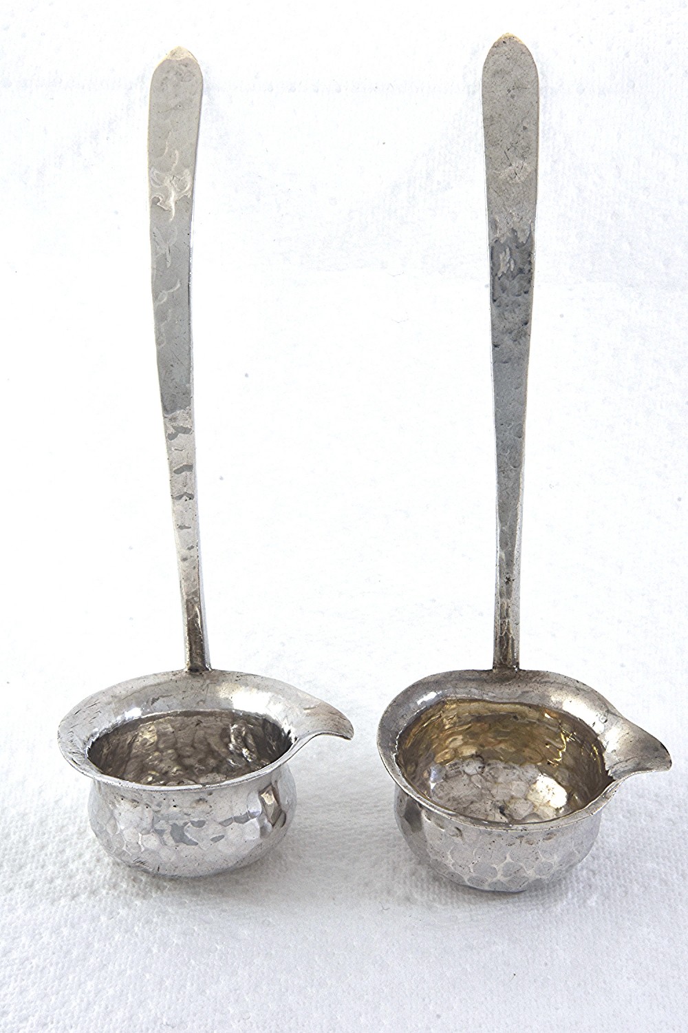 A pair of hand-hammered silver toddy ladles featuring spouted bowls and long, flattened handles.