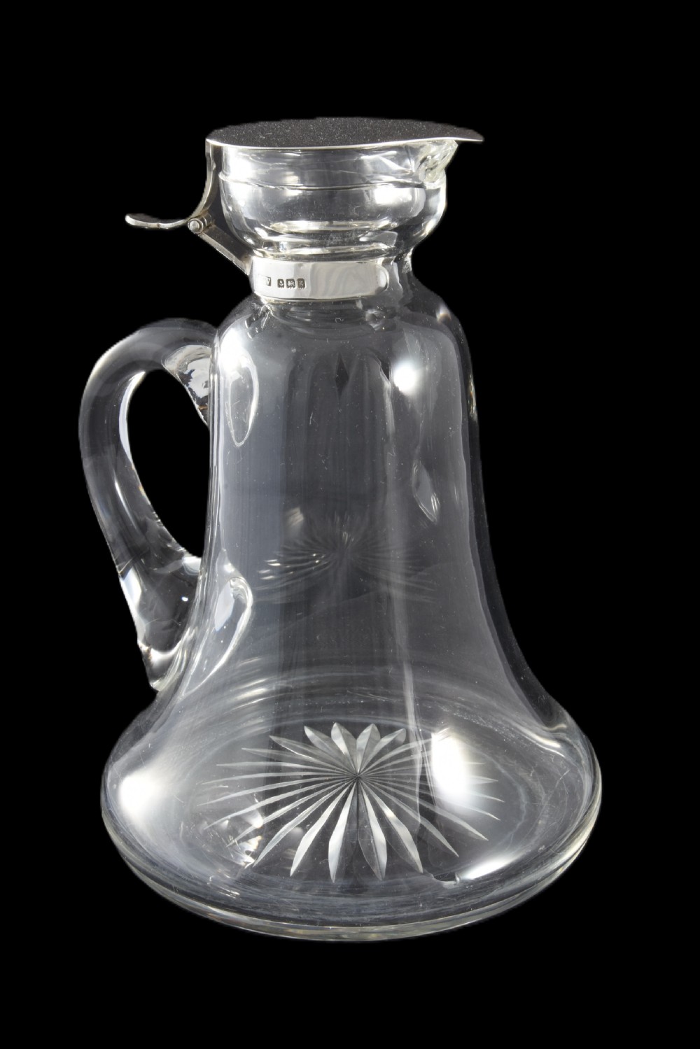 An Edwardian clear glass whisky noggin featuring a starburst cut base, applied glass loop handle, and a hallmarked sterling silver collar with a hinged lid.