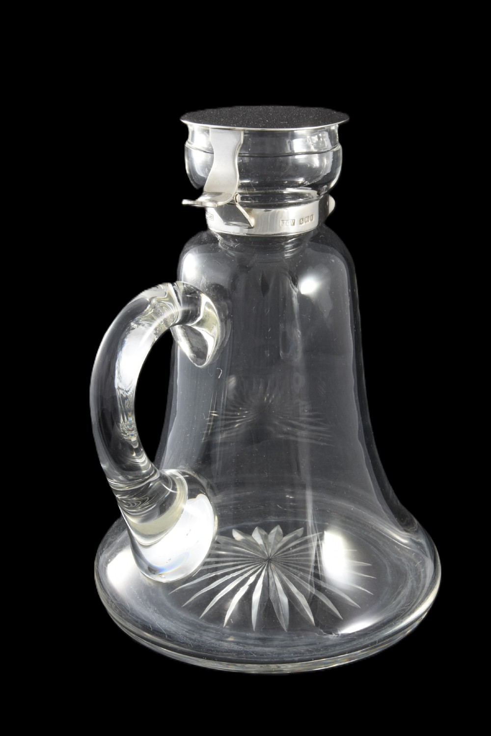 An Edwardian clear glass whisky noggin featuring a starburst cut base, applied glass loop handle, and a hallmarked sterling silver collar with a hinged lid. View II