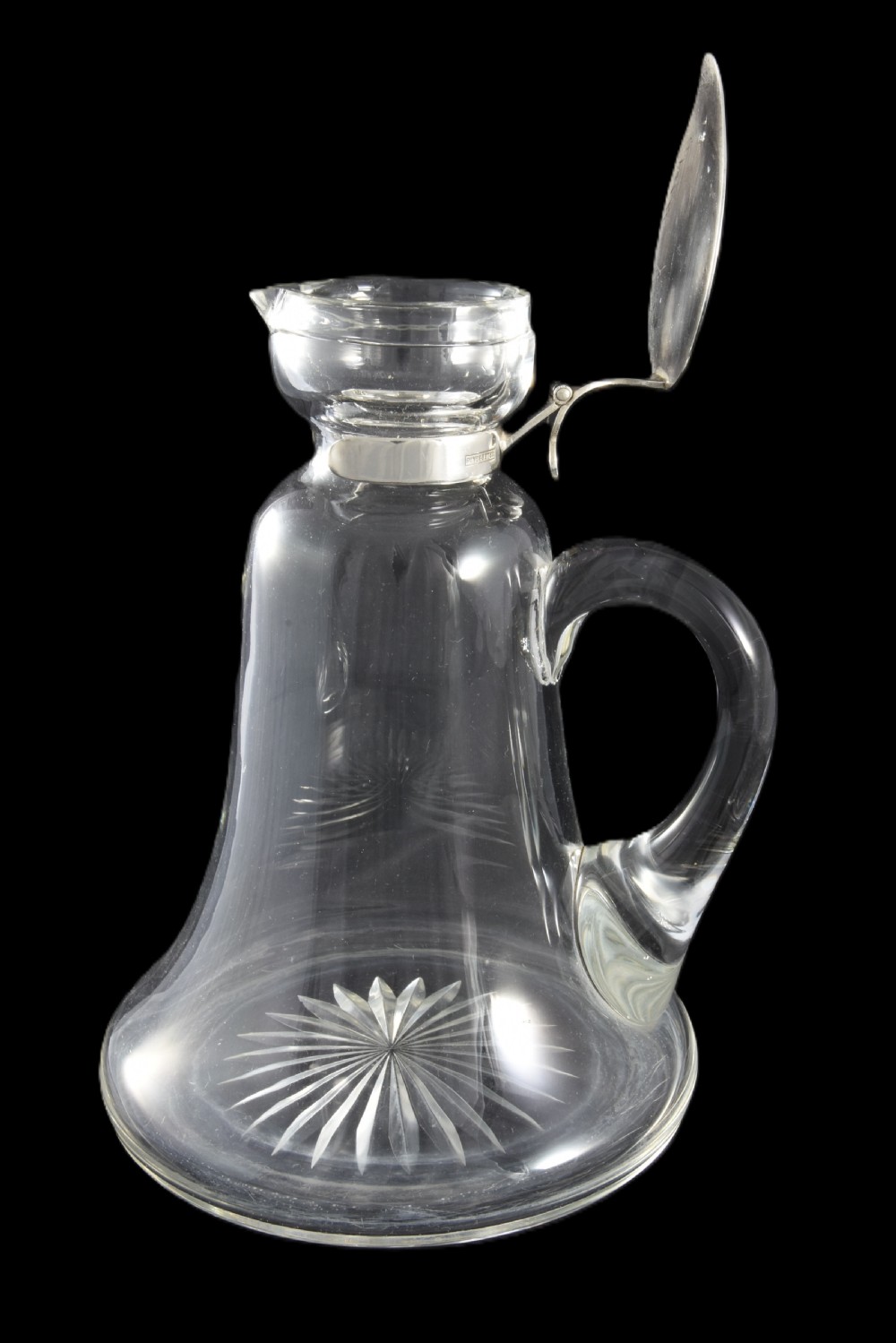 An Edwardian clear glass whisky noggin featuring a starburst cut base, applied glass loop handle, and a hallmarked sterling silver collar with a hinged lid. View III