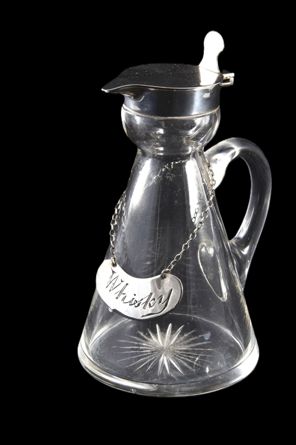 A conical clear glass whisky noggin with a starburst cut base, fitted with a silver hinged lid and an engraved silver Whisky label hanging from a chain around its neck. View II