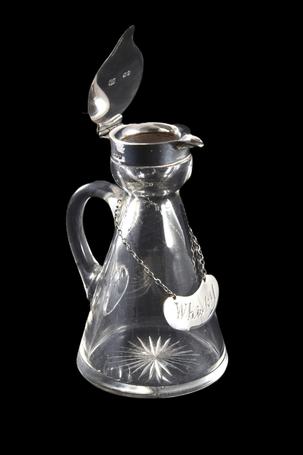 A conical clear glass whisky noggin with a starburst cut base, fitted with a silver hinged lid and an engraved silver Whisky label hanging from a chain around its neck. View V