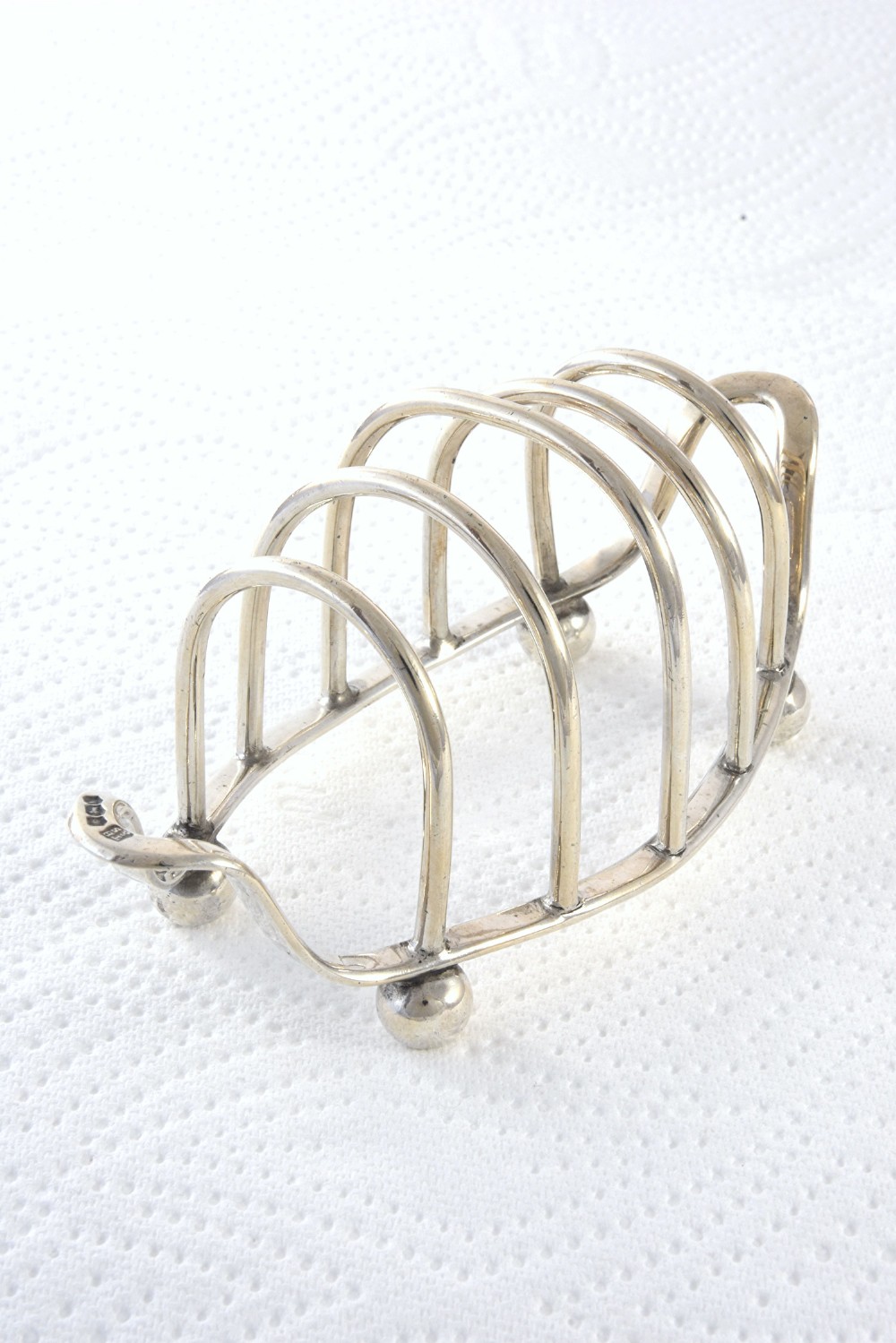 A 1939 sterling silver four-slice toast rack featuring curved wire arches, raised ball feet, and visible hallmarking.