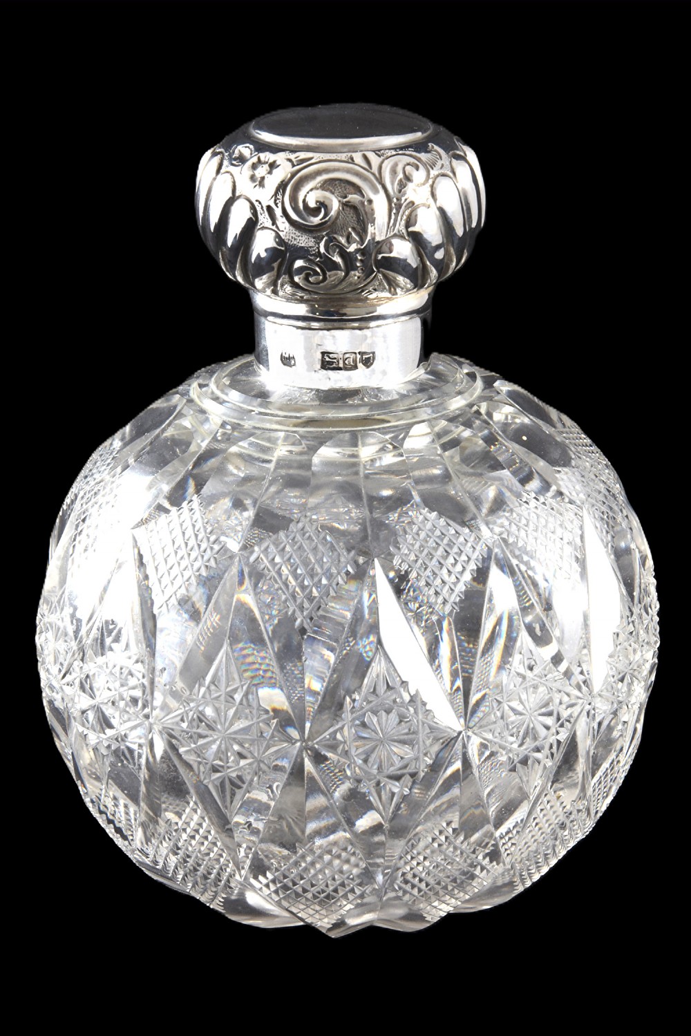 A globular cut glass scent bottle featuring geometric diamond facets topped with an embossed hallmarked sterling silver cap.