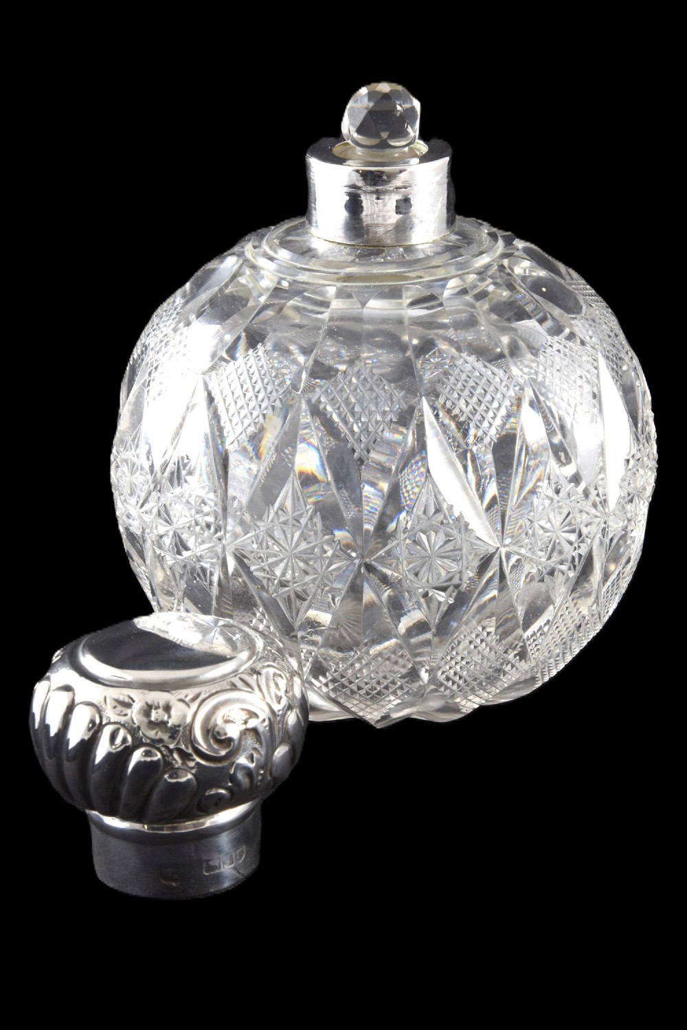 A globular cut glass scent bottle featuring geometric diamond facets topped with an embossed hallmarked sterling silver cap. View II