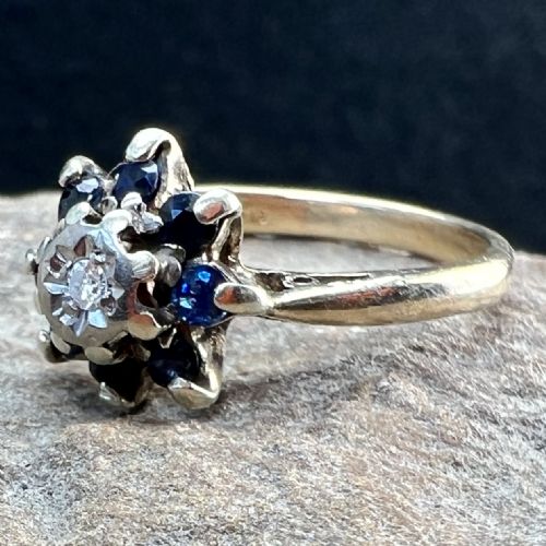 fig 1. A 9ct yellow gold ring featuring a central diamond framed by a floral cluster of dark blue sapphires.