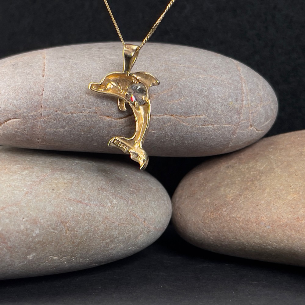 A 10ct yellow gold pendant shaped like a leaping dolphin with a brilliant-cut diamond set into its body, suspended from a gold chain. View VI
