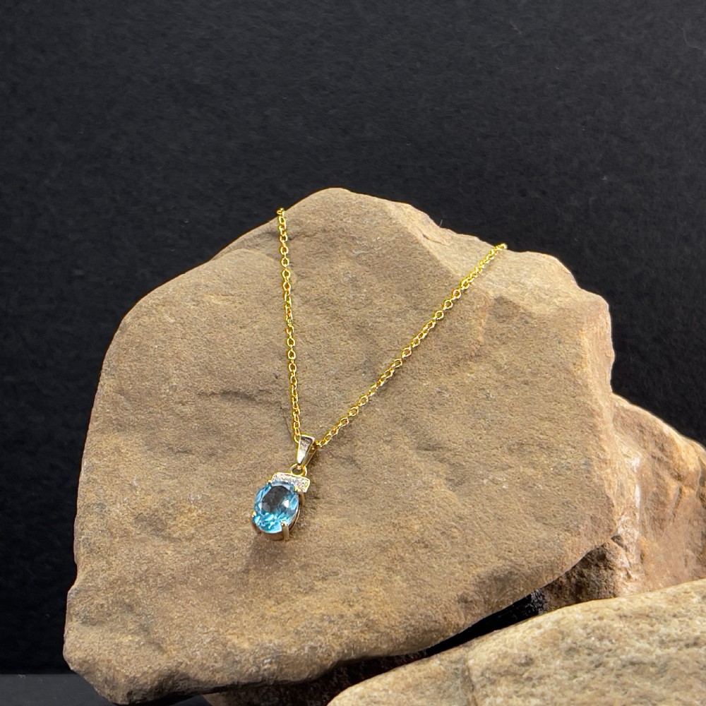 A 9ct yellow gold pendant featuring an oval faceted light blue topaz beneath a small diamond-set bar, suspended from a fine gold chain. View II