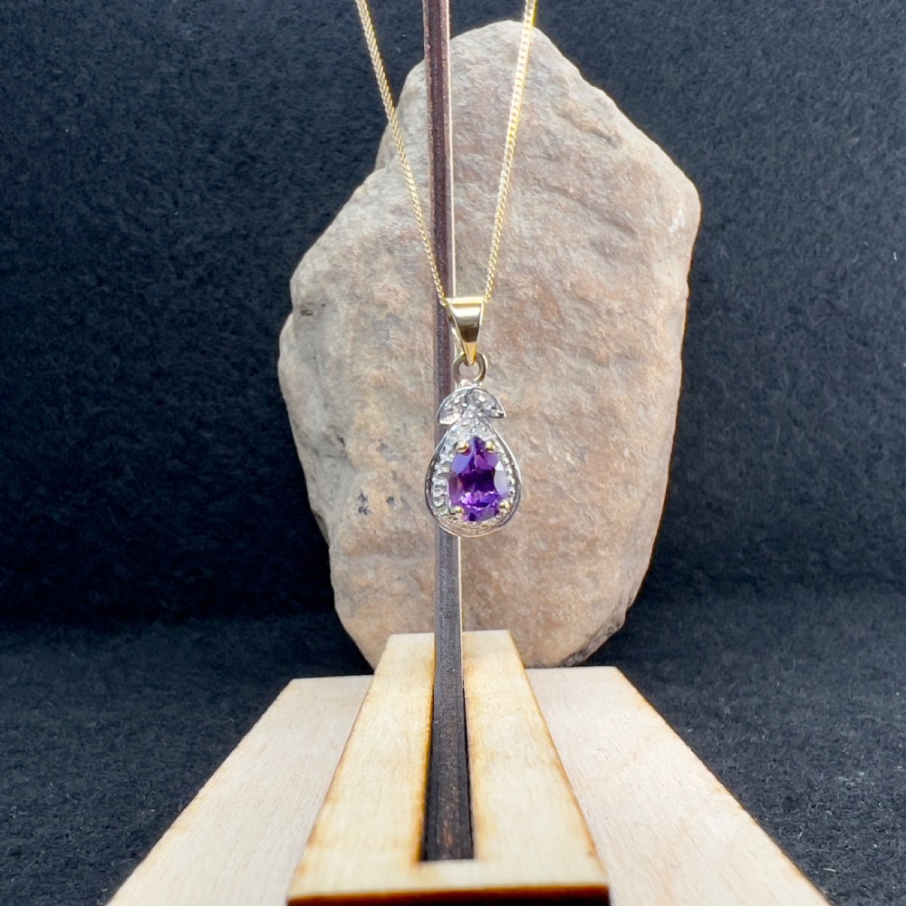 A 9ct gold teardrop pendant featuring a central oval purple amethyst set within a white metal border with accent diamonds, attached to a delicate gold chain. View X