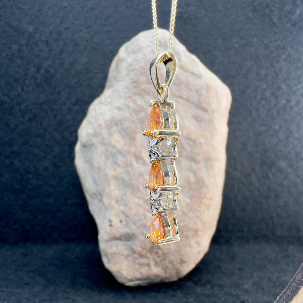 A 9ct yellow gold drop pendant featuring three pear-cut orange topaz gemstones arranged vertically with small diamond accents on a chain. View II