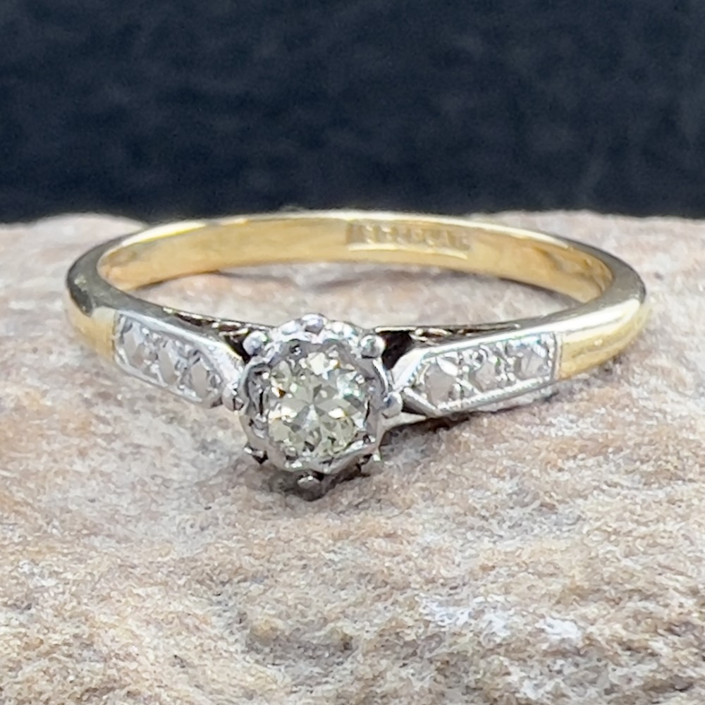 An Art Deco 18ct yellow gold and platinum solitaire ring set with a single round diamond and decorative engraved shoulders.