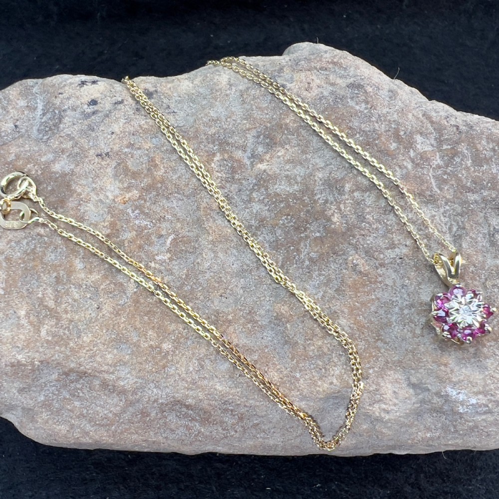 A 9ct yellow gold necklace featuring a floral starburst cluster pendant set with a central diamond surrounded by pink rubies. View XI