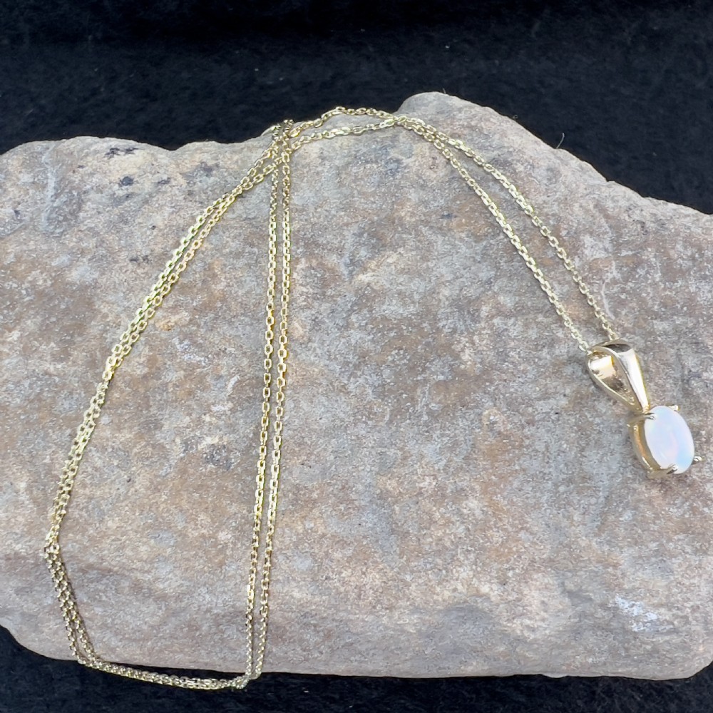 An oval white opal cabochon set in a four-claw 9ct yellow gold pendant hanging from a fine gold chain. View IX
