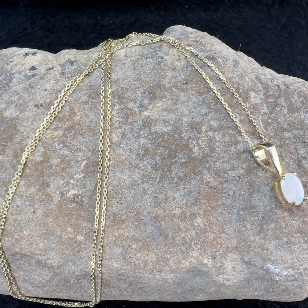An oval white opal cabochon set in a four-claw 9ct yellow gold pendant hanging from a fine gold chain. View X