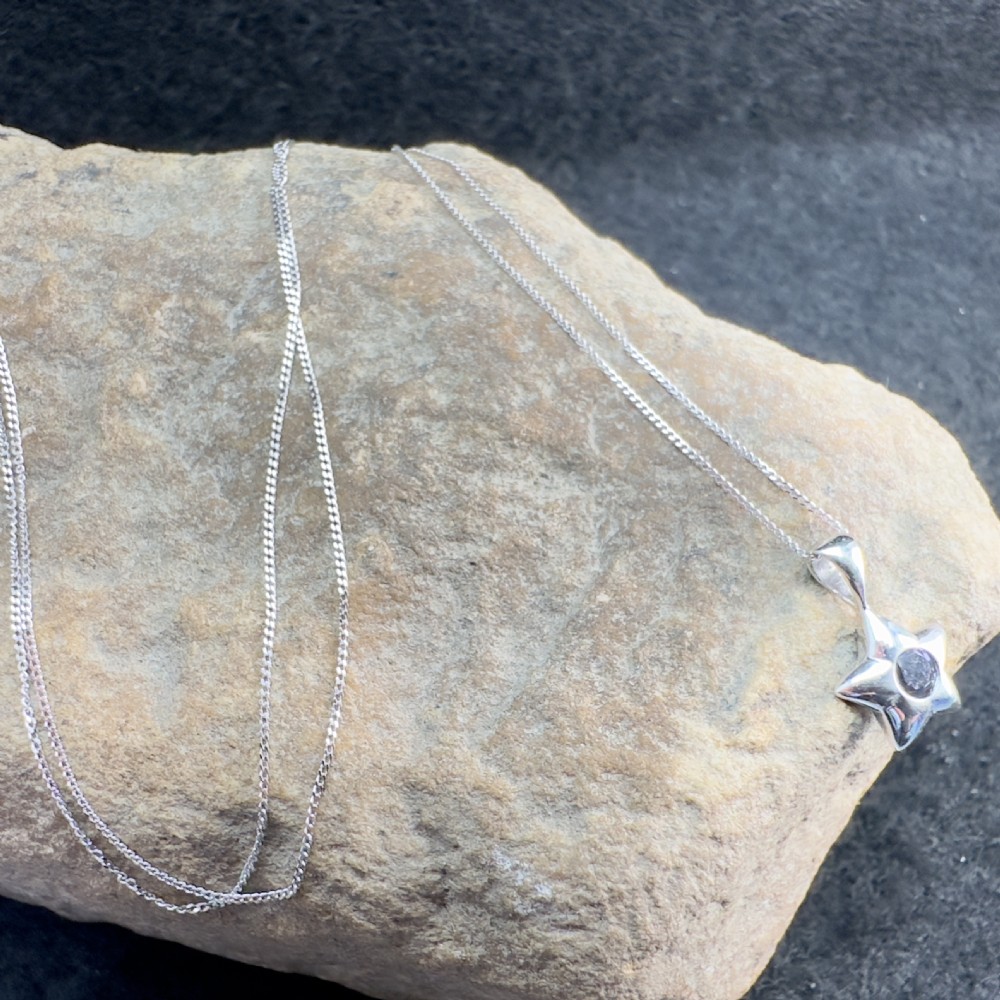 A 9ct white gold star-shaped pendant set with a central round violet iolite gemstone suspended from a fine white gold trace chain. View IX